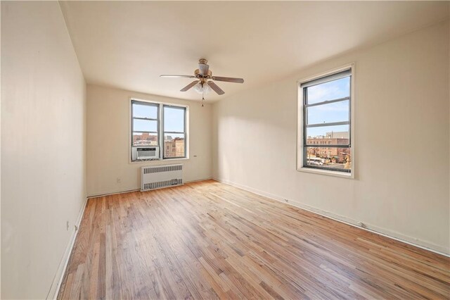 unfurnished room with cooling unit, wood finished floors, baseboards, radiator heating unit, and ceiling fan