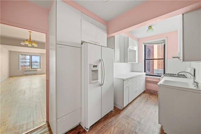 kitchen with light wood-type flooring, radiator, white fridge with ice dispenser, and white cabinetry