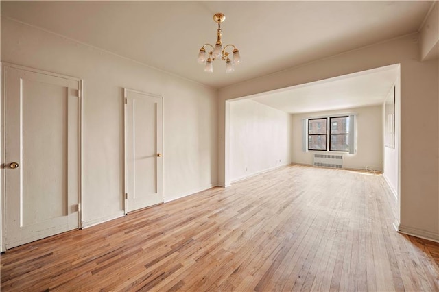 empty room featuring radiator, a notable chandelier, and light wood-style flooring