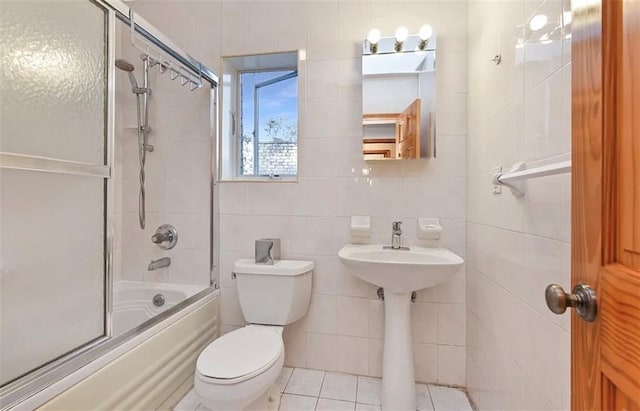 full bath with tile walls, a sink, tile patterned floors, combined bath / shower with glass door, and toilet