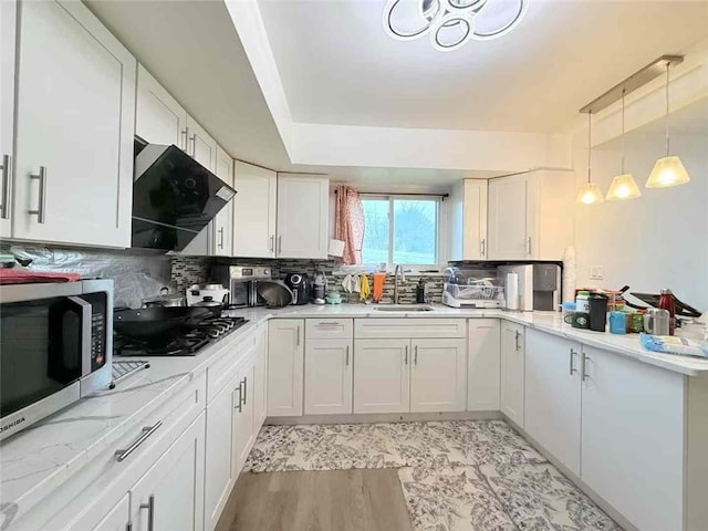 kitchen featuring white cabinets, a sink, stainless steel microwave, range hood, and stovetop