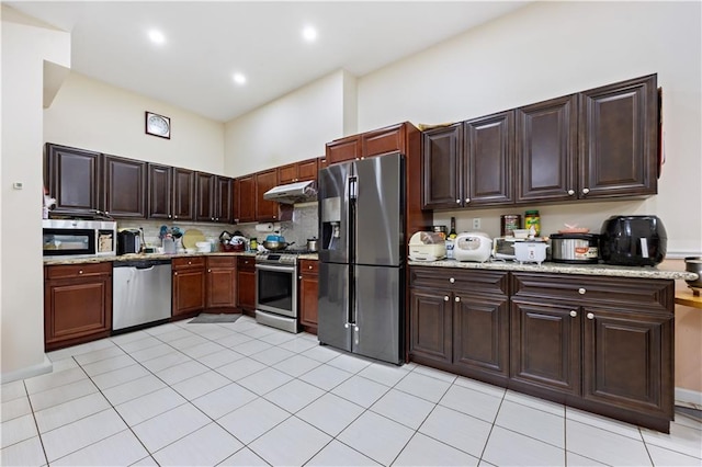 kitchen featuring stainless steel appliances, under cabinet range hood, light tile patterned flooring, tasteful backsplash, and dark brown cabinets