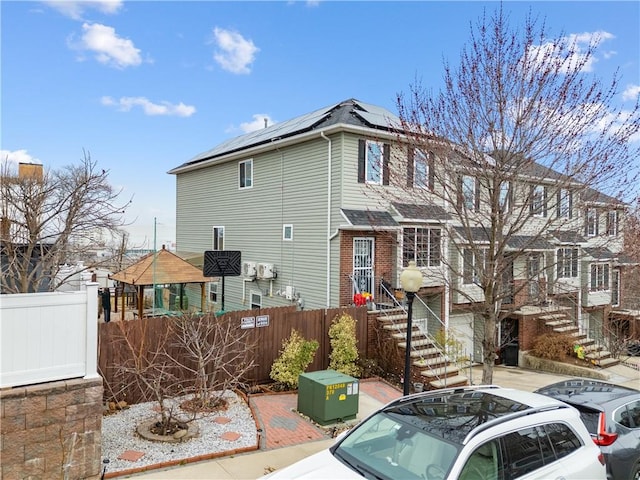 view of front of property featuring roof mounted solar panels, stairway, a shingled roof, and fence