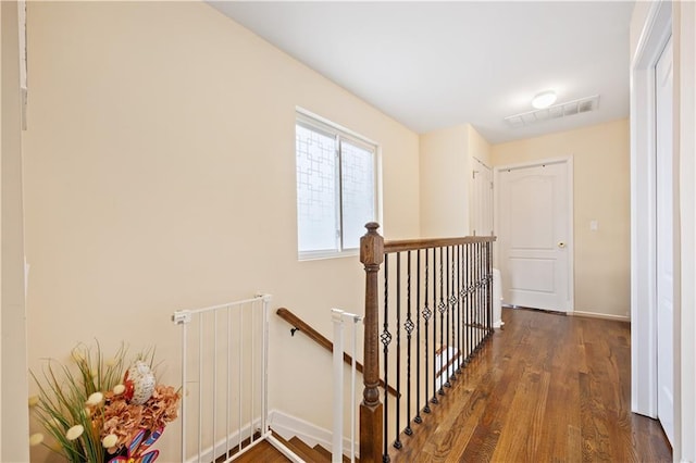 hallway with an upstairs landing, visible vents, wood finished floors, and baseboards