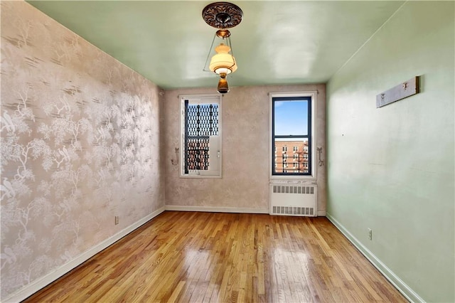unfurnished room featuring hardwood / wood-style floors, baseboards, and radiator