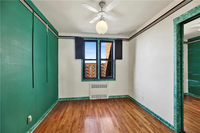 unfurnished room featuring baseboards, wood finished floors, ceiling fan, and radiator