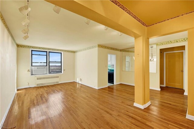 empty room with rail lighting, radiator heating unit, hardwood / wood-style flooring, and baseboards