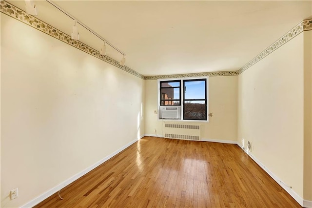 empty room featuring track lighting, radiator, hardwood / wood-style flooring, and baseboards