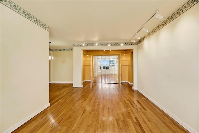 corridor with baseboards, rail lighting, and wood-type flooring