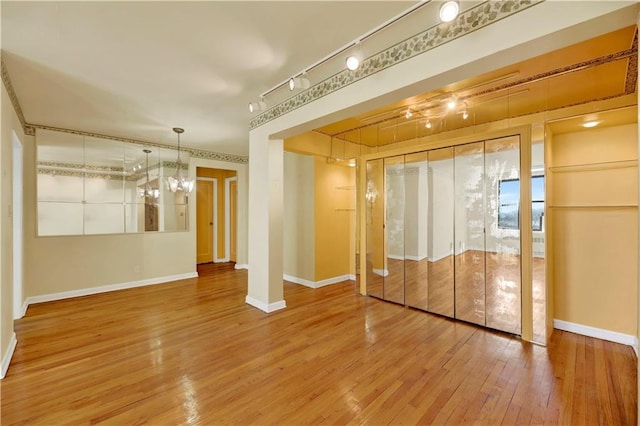 interior space with an inviting chandelier, baseboards, track lighting, and wood-type flooring