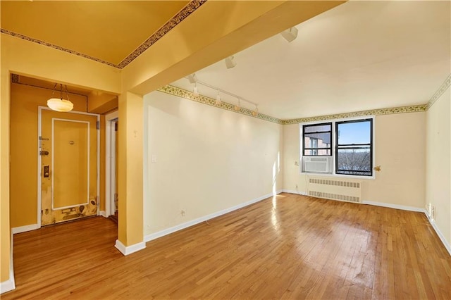 empty room with radiator heating unit, cooling unit, track lighting, wood-type flooring, and baseboards