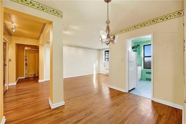 unfurnished dining area with baseboards, radiator, an inviting chandelier, and light wood finished floors