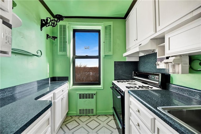 kitchen featuring radiator heating unit, white cabinetry, gas stove, and under cabinet range hood