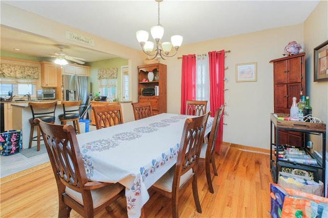 dining room featuring a chandelier, light wood-style floors, baseboards, and a ceiling fan