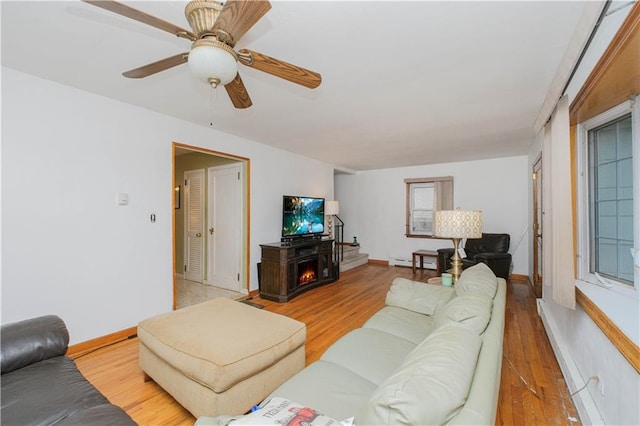 living area featuring a baseboard heating unit, light wood finished floors, a ceiling fan, and baseboards