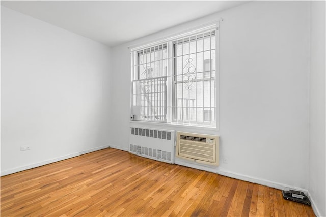 empty room with radiator, light wood-style floors, baseboards, and a wall mounted air conditioner