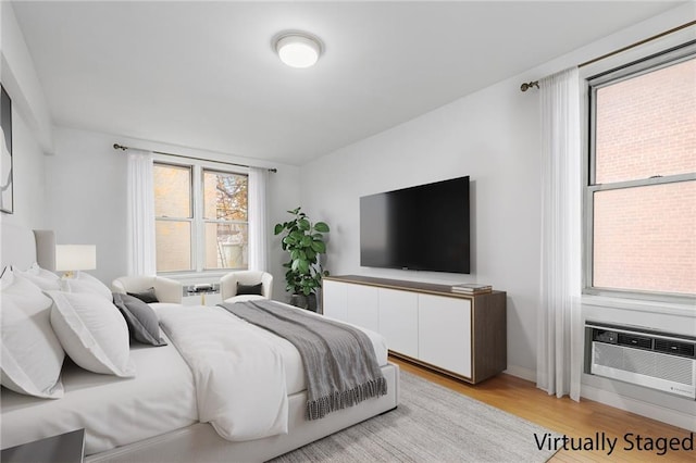 bedroom with baseboards, a wall unit AC, and light wood-type flooring