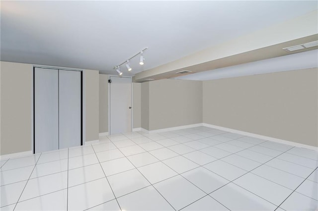finished below grade area featuring baseboards, visible vents, and track lighting