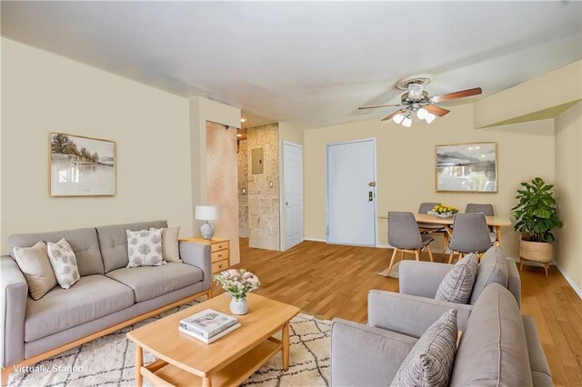 living area featuring baseboards, light wood-style floors, and ceiling fan