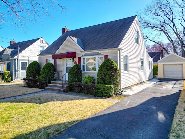 cape cod-style house featuring a detached garage, an outdoor structure, a front lawn, a chimney, and driveway