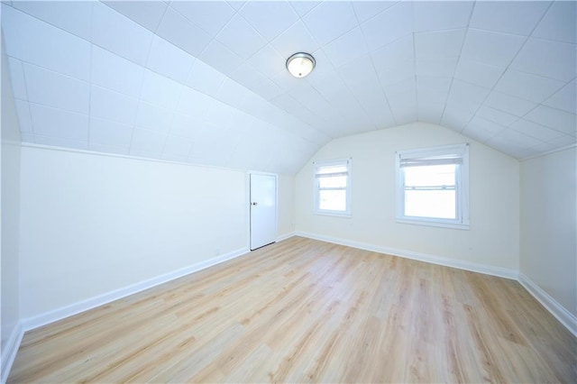 additional living space featuring light wood finished floors, baseboards, and vaulted ceiling