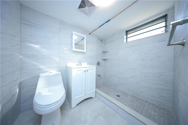 bathroom with a tile shower, vanity, visible vents, toilet, and tile walls