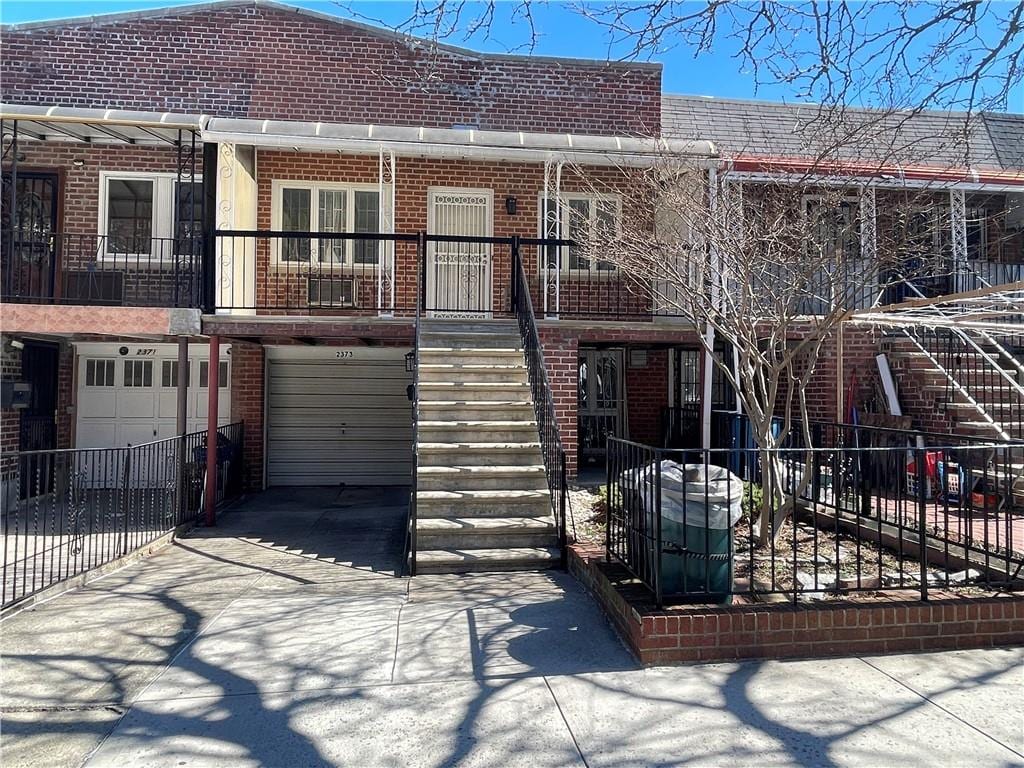 multi unit property with concrete driveway, stairs, brick siding, and an attached garage