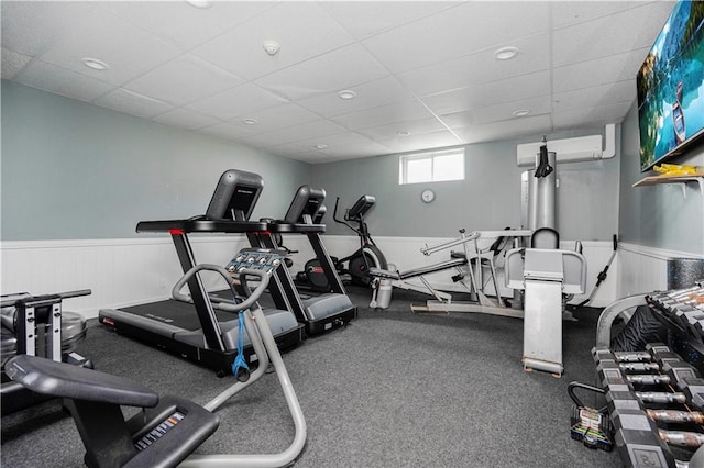 workout area featuring a drop ceiling, a wainscoted wall, and a wall mounted air conditioner