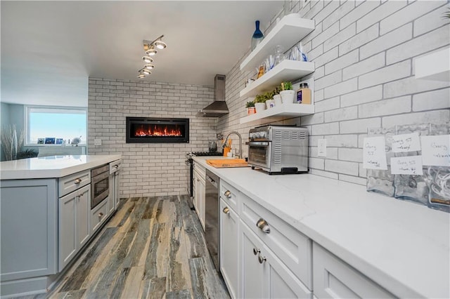 kitchen with wall chimney exhaust hood, dark wood-style flooring, brick wall, a fireplace, and a sink