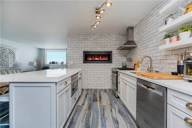 kitchen with stainless steel appliances, wall chimney exhaust hood, open floor plan, dark wood finished floors, and light countertops