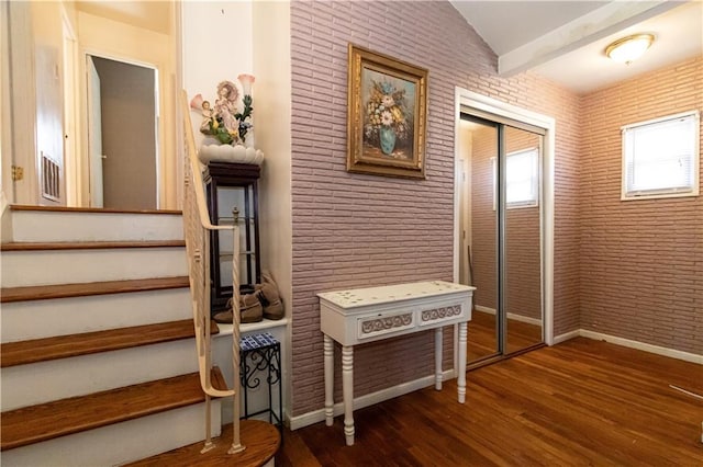 stairway with wood finished floors, vaulted ceiling, brick wall, and baseboards