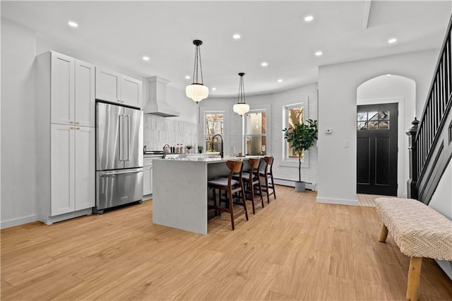 213 E 9th St, Brooklyn, NY 11218 - kitchen with high end fridge, wall chimney exhaust hood, a kitchen island with sink, recessed lighting, and light wood-type flooring