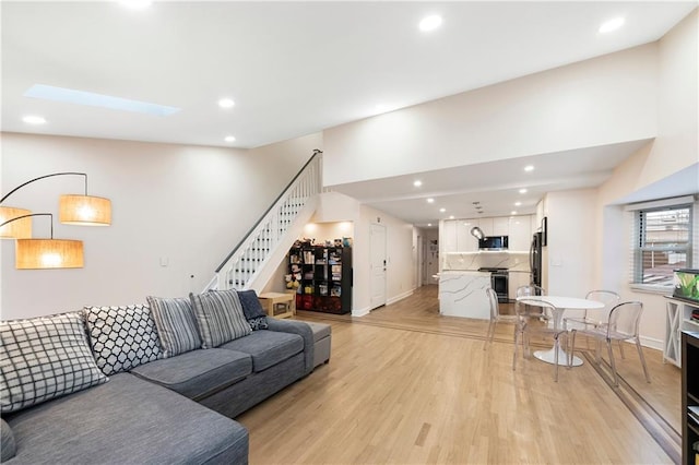 living room with light wood finished floors, stairs, recessed lighting, baseboards, and a skylight