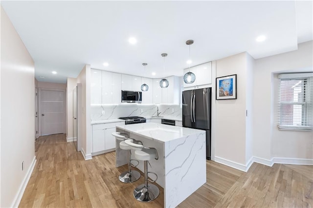 kitchen featuring freestanding refrigerator, stainless steel microwave, white cabinetry, a kitchen island, and light wood-type flooring