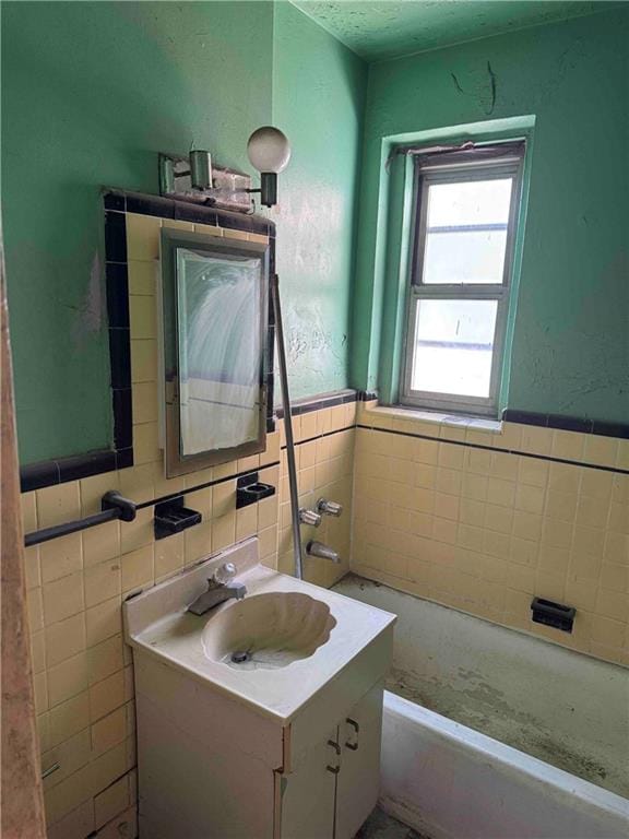 bathroom with a bath, wainscoting, vanity, and tile walls