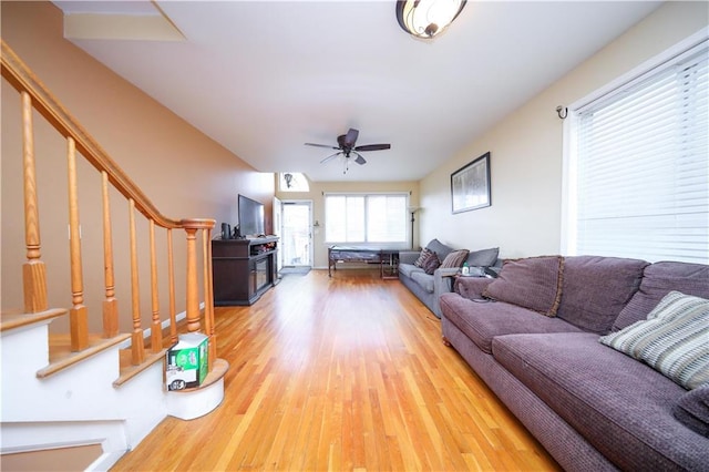 living area with stairs, a ceiling fan, and wood finished floors