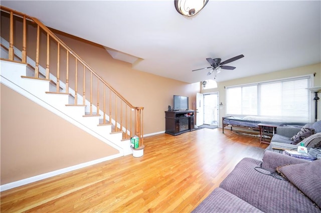 living area with wood finished floors, baseboards, a ceiling fan, and stairs