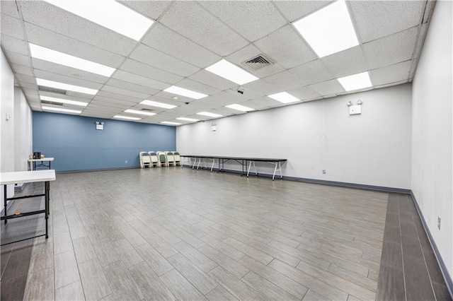 unfurnished room featuring baseboards, visible vents, a drop ceiling, and wood finished floors
