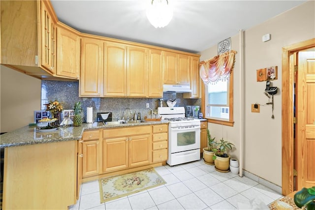 kitchen featuring white gas stove, a sink, under cabinet range hood, light brown cabinets, and decorative backsplash