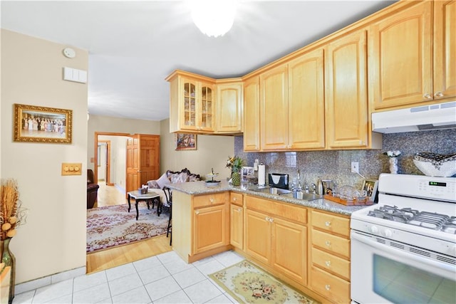 kitchen featuring white range with gas stovetop, under cabinet range hood, light brown cabinets, light tile patterned floors, and tasteful backsplash