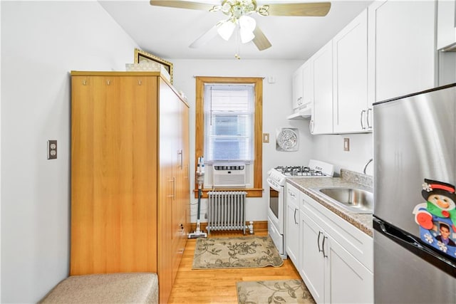 kitchen with stainless steel refrigerator, radiator heating unit, white gas stove, a sink, and cooling unit