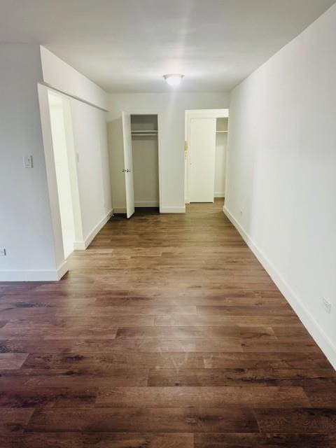 unfurnished bedroom with dark wood-type flooring, two closets, and baseboards