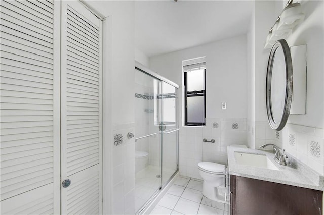 bathroom with a closet, a stall shower, toilet, and tile walls