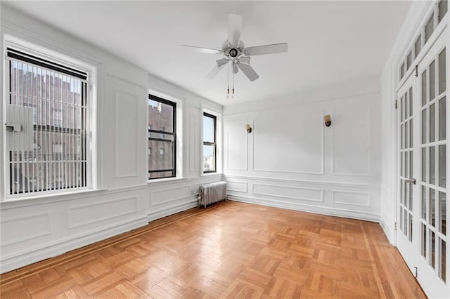 unfurnished room with a ceiling fan, radiator heating unit, and a decorative wall
