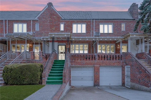 view of property with a garage, brick siding, concrete driveway, and stairs