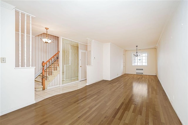 spare room featuring a chandelier, radiator, wood finished floors, stairs, and ornamental molding