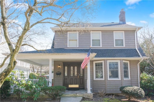 view of front of home featuring a shingled roof, covered porch, and a chimney