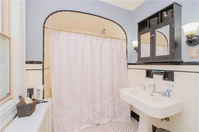 bathroom with a shower with curtain, a sink, wainscoting, and tile walls