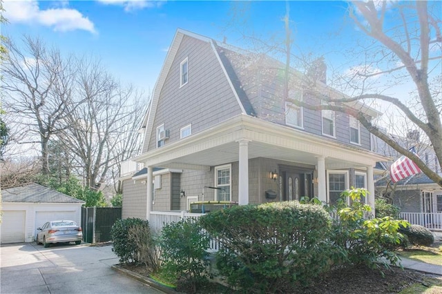 view of front facade with a gambrel roof, a detached garage, an outdoor structure, a porch, and a chimney