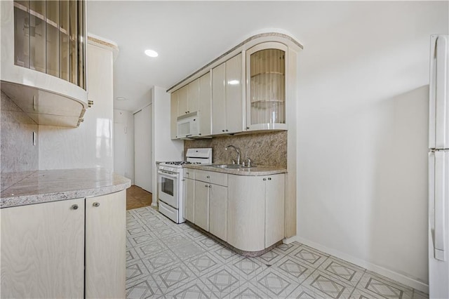 kitchen with white appliances, glass insert cabinets, light countertops, tasteful backsplash, and a sink